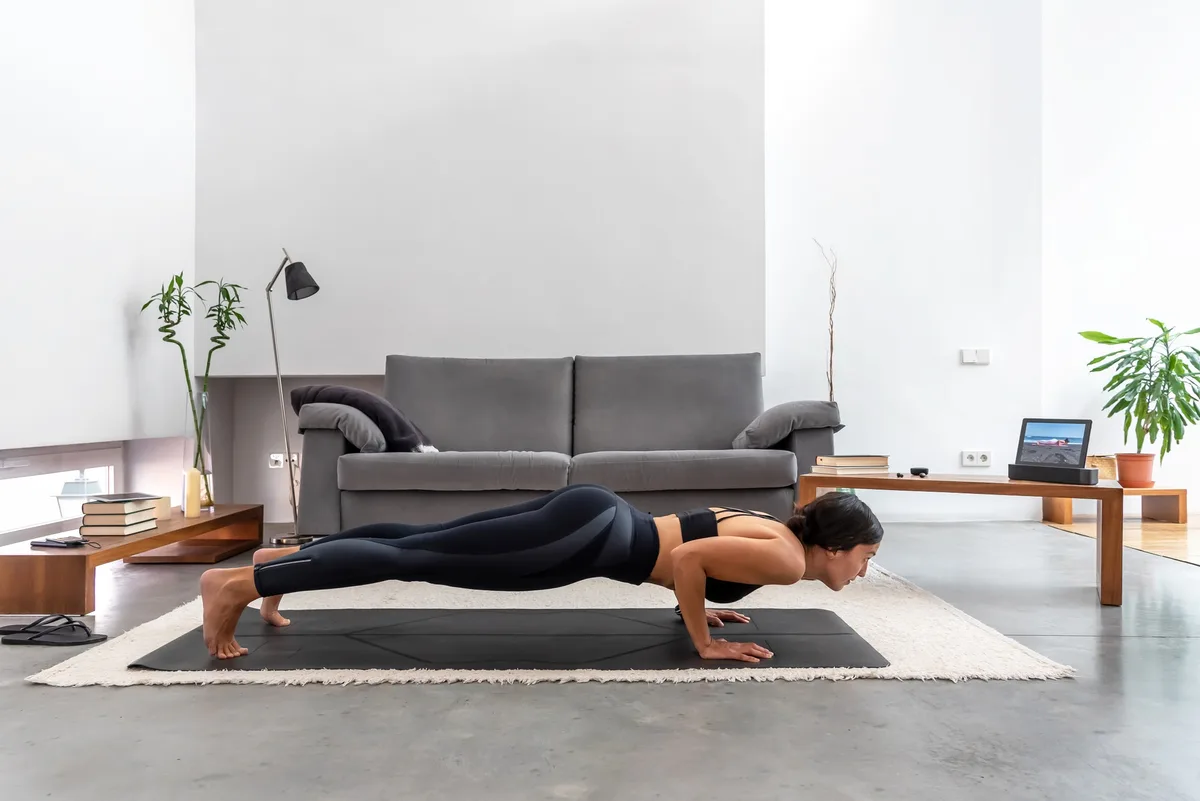 Fit woman practicing Chaturanga pose using online yoga training program in the tablet at home
