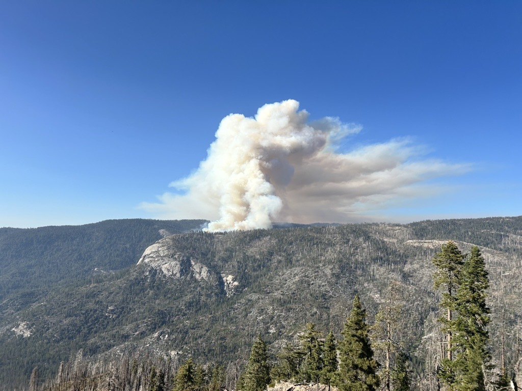 Una columna de humo se eleva desde un bosque de Yosemite, vista a distancia desde Wawona Point.